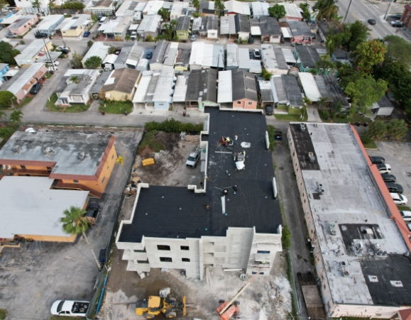 Aerial view of a commercial building under construction showing black flat roof installation in an urban area.