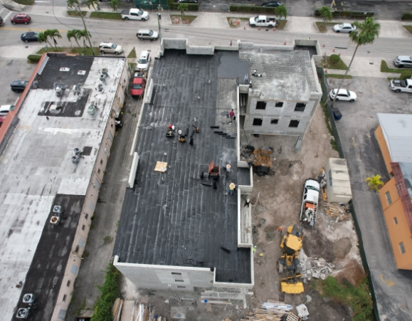 Aerial overhead view of workers installing a black torch-down modified bitumen membrane on a commercial building roof.