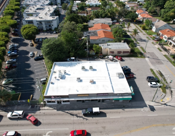 High-angle aerial view of a commercial strip mall featuring a white TPO flat roof system and rooftop HVAC units.