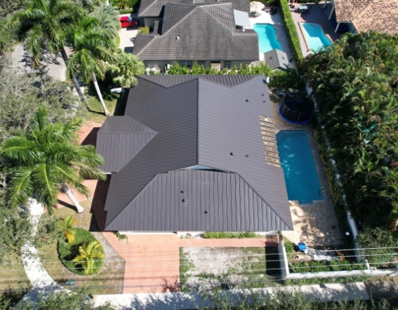 Aerial view of a single-family home featuring a newly installed dark gray standing seam metal roof and swimming pool.