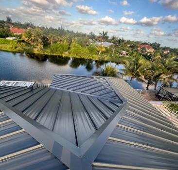Close-up aerial view of a dark gray standing seam metal roof installation overlooking a lake.