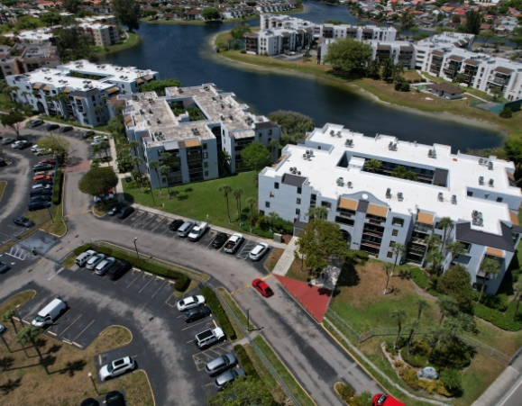 Aerial perspective of a multi-building lakeside apartment complex featuring bright white commercial flat roofs.