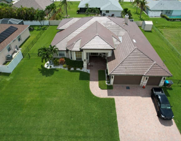Aerial shot of a modern single-story residence with a beige concrete tile roof and paved driveway.