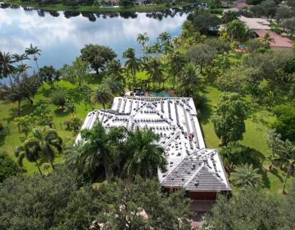High-angle aerial view of a large luxury estate undergoing roof tile installation with white underlayment near a lake.