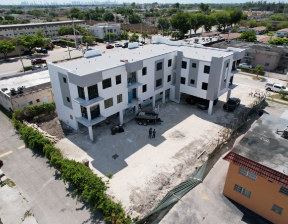 Aerial view of a modern multi-story apartment building with a white flat roof under construction.