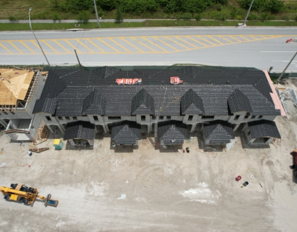 Aerial overhead view of a newly built multi-family townhouse complex with dark gray tile roofs along a main road.