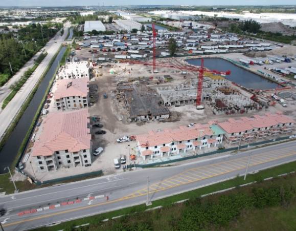 Wide aerial view of a large multi-family housing development under construction with red tower cranes.