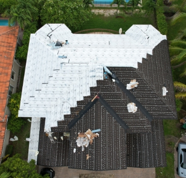 Top-down aerial view of a residential roof halfway through installing white synthetic underlayment over black felt paper.