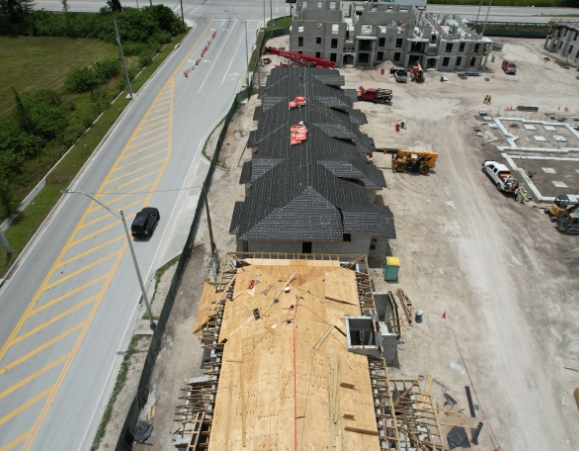 Aerial view of a townhouse development under construction showing plywood roof decking and black roofing underlayment.